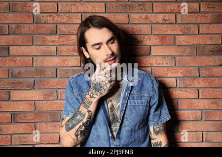 Giovane uomo con tatuaggi sul corpo vicino al muro di mattoni Foto Stock
