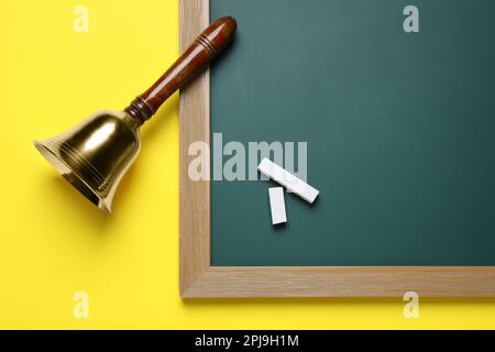 Campana d'oro, tavola verde e gesso su fondo giallo, giacitura piatta. Giornate scolastiche Foto Stock