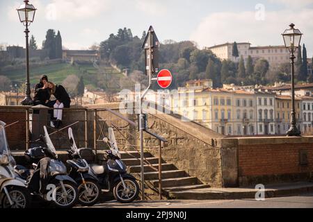 Una giovane coppia prende un selfie al telefono mentre si siede accanto al fiume Arno a Firenze Foto Stock