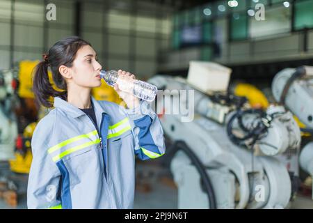 assistenza sanitaria donna lavoratore bere acqua pulita mentre si lavora in fabbrica macchina magazzino per rinfresco e personale sano Foto Stock