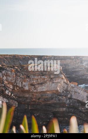 L'escursionista celebra il suo successo. Scogliere mozzafiato con spiaggia di ciottoli nel sole pomeridiano sulla costa atlantica a Vila Nova de Milfontes, Odemira, Por Foto Stock
