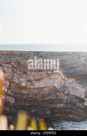 L'escursionista celebra il suo successo. Scogliere mozzafiato con spiaggia di ciottoli nel sole pomeridiano sulla costa atlantica a Vila Nova de Milfontes, Odemira, Por Foto Stock