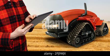 Un agricoltore con tablet digitale controlla un trattore autonomo in un'azienda agricola intelligente. Foto di alta qualità Foto Stock