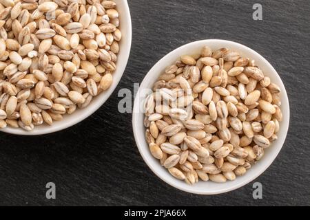 Orzo perlato biologico in piattini di ceramica bianca su pietra ardesia, primo piano, vista dall'alto. Foto Stock