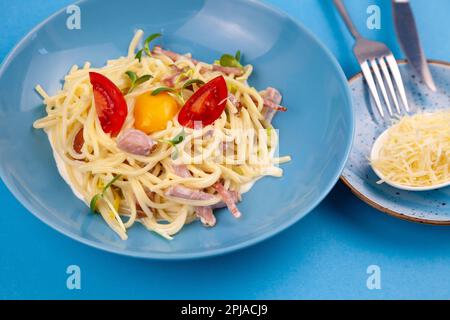 Pasta con formaggio e uova, pancetta e pomodori, microgreens. Cibo in un piatto blu. Pasta di carbonara fatta in casa. Pranzo sul tavolo con vista. Spaghetti italiani con prosciutto, panna Foto Stock