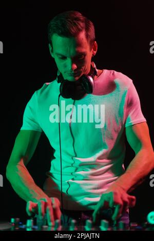 Ritratto del giovane DJ mixare musica in festa in luce verde. Persona maschile cool che si esibisce sul palco come un disco di jockey Foto Stock