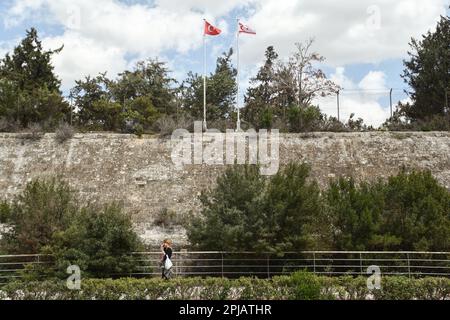 Nicosia, Nicosia, Cipro. 1st Apr, 2023. Una donna cammina davanti alle bandiere della Turchia e la cosiddetta "Repubblica turca di Cipro del Nord” sventola sulle vecchie mura di Nicosia. Il ministero degli Affari esteri di Cipro ha rilasciato una dichiarazione relativa alle opere all'interno della zona cuscinetto, dove la cosiddetta "Repubblica turca di Cipro del Nord” sta costruendo uno stadio di calcio. La zona cuscinetto è il suolo cipriota che viene donato volentieri alle Nazioni Unite per aver facilitato il suo dovere di mantenimento della pace e, secondo la dichiarazione, il governo cipriota non ha mai concesso alcuna autorizzazione per lavori all'interno della zona cuscinetto e della domanda Foto Stock