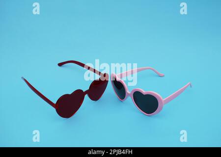 Occhiali rossi e rosati a forma di cuore su sfondo di carta blu. Due occhiali glamour a forma di cuore. Foto Stock