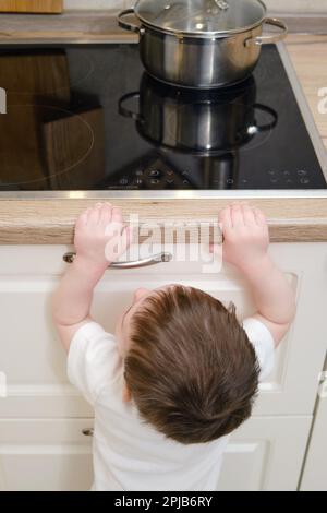 Il bambino salite su una stufa elettrica calda nella cucina domestica. Un bambino piccolo tocca la superficie della stufa con la mano al rischio di ottenere b Foto Stock