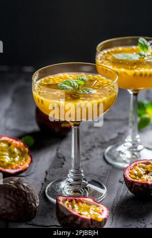 Cocktail alcolico o analcolico con frutta fresca di passione (maracuya) e menta su fondo nero Foto Stock