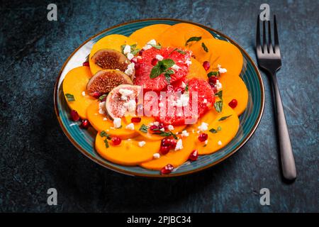 Insalata invernale sana - insalata di carpaccio di Persimmon con melograno, formaggio feta, pompelmo rosa e fichi Foto Stock