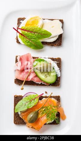 Variazione di panini sani aperti sul pane di Pumpernickel con verdure, salmone, prosciutto, erbe e formaggio morbido Foto Stock