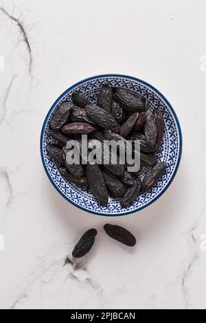 Fagioli tonka profumati (Dipteryx odorata) in una piccola ciotola su fondo bianco, ingrediente aromatizzato alla cottura Foto Stock