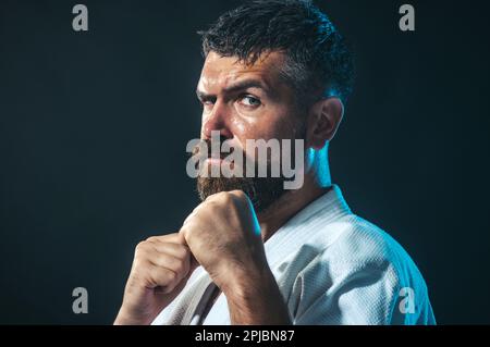 Uomo allenamento karate in palestra. Concetto di sport e fitness. Combattente di arti marziali. Uomo barbuto in kimono bianco per sambo, judo, jujitsu con mani appese Foto Stock