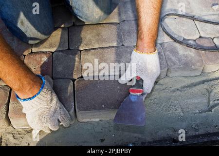 Addetto alle costruzioni che fissa la pietra da pavimento sul lavoratore della strada che installa blocchi di pietra sui marciapiedi Foto Stock