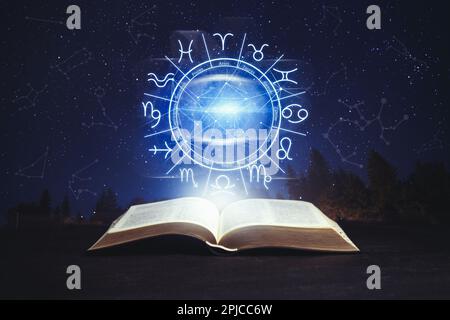 Vecchio libro sulla superficie nera e illustrazione della ruota zodiacale con segni astrologici sotto il cielo stellato di notte Foto Stock