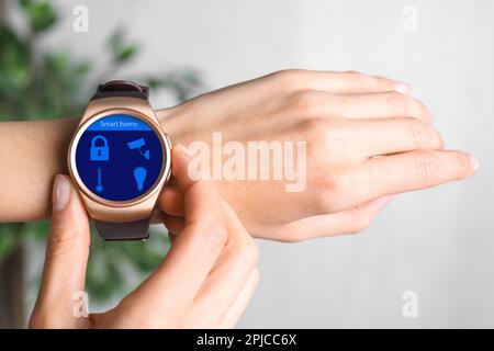 Giovane donna controllo orologio da polso elettronico con Smart Home Interface per interni, primo piano Foto Stock