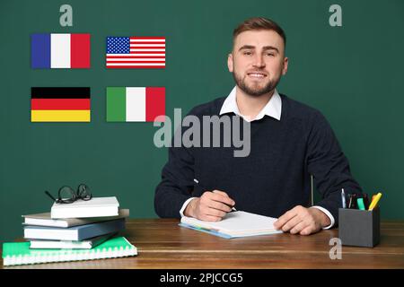 Ritratto dell'insegnante di lingue straniere a tavola di legno e diverse bandiere di lavagna verde Foto Stock