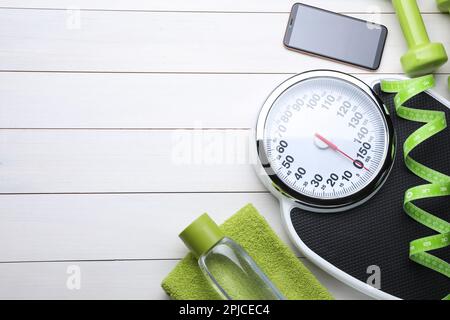 Composizione piatta con scala da bagno e metro a nastro su pavimento in legno bianco, spazio per testo. Concetto di perdita del peso Foto Stock