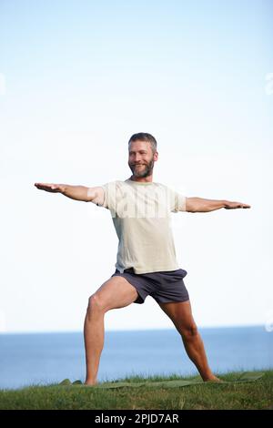 Guerriero in natura. Scatto completo di un bell'uomo maturo che fa yoga all'aperto. Foto Stock