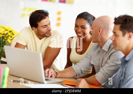 Shes il loro miglior giocatore di squadra. Un bel giovane che mostra ai suoi colleghi qualcosa su un notebook davanti a loro. Foto Stock