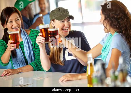 Un altro. Tre amiche che si tirano indietro con qualche drink al bar e guardano lo sport. Foto Stock