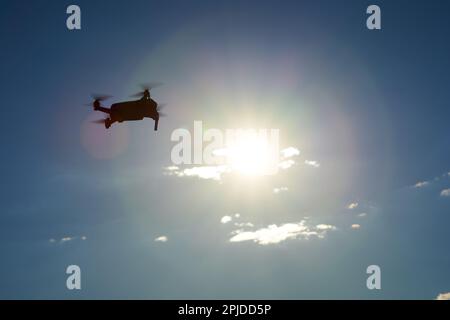 Drone scuro dal lato come silhouette. Sole giallo di fronte al cielo blu scuro con nuvole bianche. Vista in alto. Foto Stock