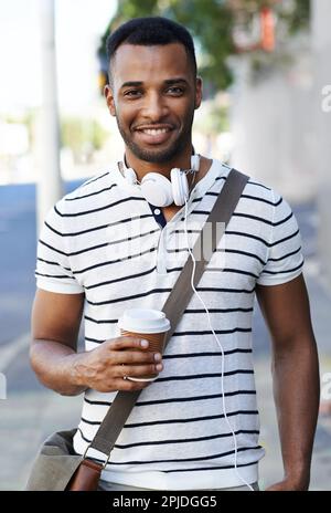 L'uomo urbano perfetto. Un bell'uomo d'affari afro-americano vestito casualmente in città con le sue cuffie intorno al collo. Foto Stock