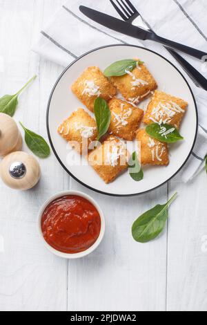 Ravioli fritti croccanti con spinaci e formaggio serviti con salsa marinara primo piano su un piatto su un tavolo di legno. Vista verticale dall'alto Foto Stock