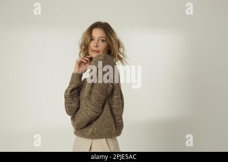 Ritratto di moda di giovane donna in maglione invernale marrone e pantaloni larghi beige su sfondo bianco Foto Stock