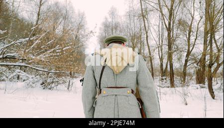 Gli uomini vestiti come soldati della Guardia Bianca dell'esercito imperiale russo nella marcia della Guerra civile Russa attraverso la foresta invernale innevata. Rievocazione storica Foto Stock