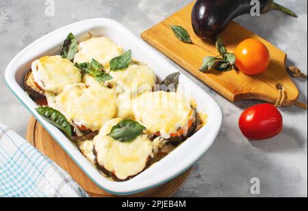 Melanzane cotte con mozzarella, pomodori in teglia su un tavolo di cemento. Ricetta vegetariana Foto Stock