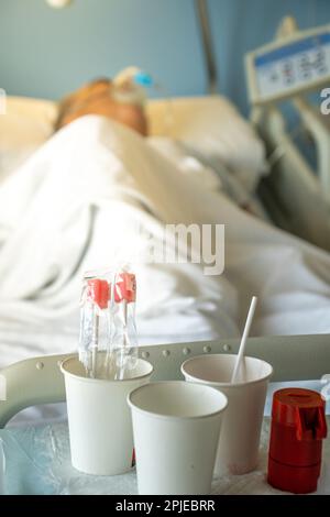 Tavolo della stanza dell'ospedale con vasi e medicine per infermieri e pazienti anziani in un letto dell'ospedale che indossa la maschera dell'ossigeno del sistema medico respiratorio per il chron Foto Stock