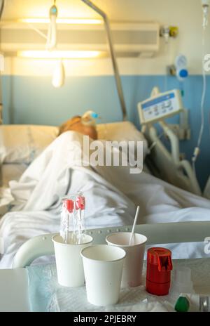 Tavolo della stanza dell'ospedale con vasi e medicine per infermieri e pazienti anziani in un letto dell'ospedale che indossa la maschera dell'ossigeno del sistema medico respiratorio per il chron Foto Stock