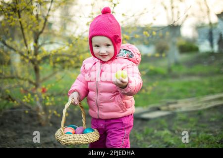 Il bambino raccoglie le uova di Pasqua colorate nel cestino. Concetto di caccia all'uovo di Pasqua. Foto Stock