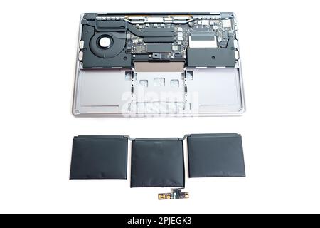 La batteria, che si è espansa a causa di problemi interni, viene posizionata accanto a un computer portatile smontato isolato su sfondo bianco. Manutenzione hardware e REP Foto Stock