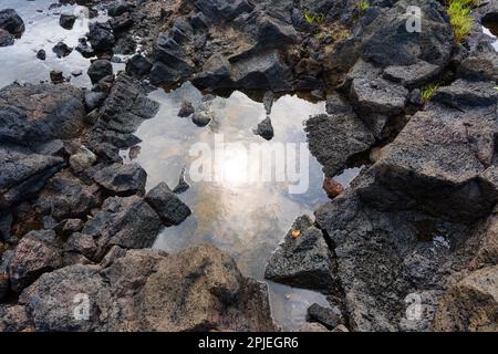 Bellezza e potenza del mondo naturale delle Hawaii mentre i raggi del sole si riflettono sulle piscine di marea dell'oceano formate nelle fessure rocciose delle rocce laviche. Foto Stock