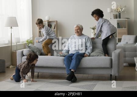 Tre diversi nipoti attivi che corrono intorno a un allegro nonno più anziano Foto Stock