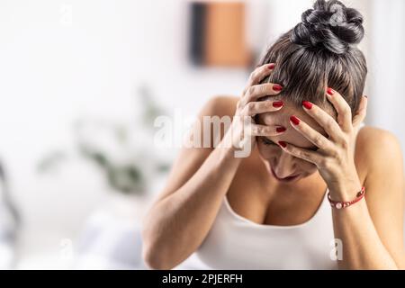 Donna stressata ed esausta con migrene tiene la testa nelle mani dall'angoscia. Foto Stock