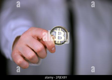 Un uomo d'affari in una camicia bianca e cravatta nera tiene una versione fisica di bitcoin nelle sue mani. Foto Stock