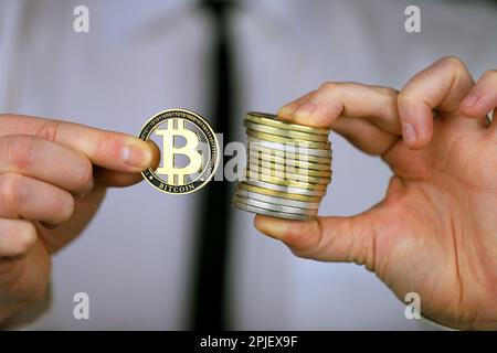 Un uomo d'affari in una camicia bianca e cravatta nera tiene una versione fisica di bitcoin nelle sue mani. Foto Stock