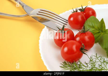 Pomodori ciliegini su un piatto con basilico e posate. Cibo di dieta Foto Stock