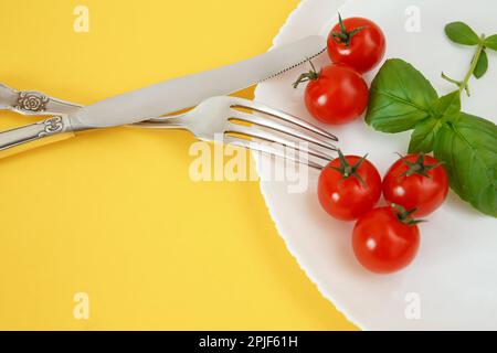 Pomodori ciliegini su un piatto con basilico e posate. Cibo di dieta Foto Stock