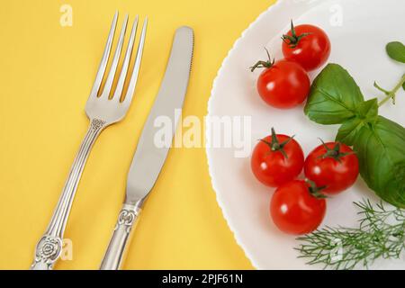 Pomodori ciliegini su un piatto con basilico e posate. Cibo di dieta Foto Stock