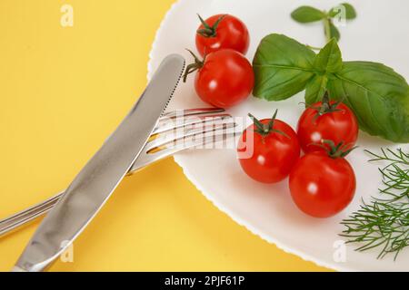 Pomodori ciliegini su un piatto con basilico e posate. Cibo di dieta Foto Stock