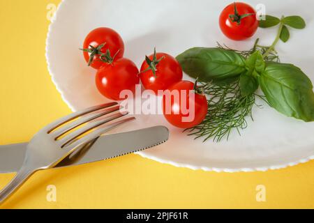 Pomodori ciliegini su un piatto con basilico e posate. Cibo di dieta Foto Stock