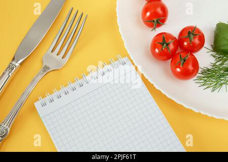 Pomodori ciliegini su un piatto con basilico e posate. Notebook per la registrazione e il conteggio delle calorie alimenti dietetici Foto Stock