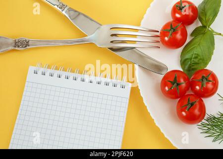 Pomodori ciliegini su un piatto con basilico e posate. Notebook per la registrazione e il conteggio delle calorie alimenti dietetici Foto Stock