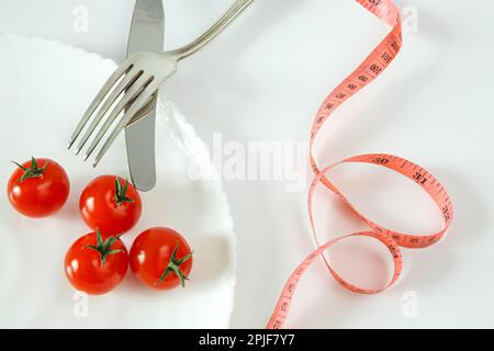 Pomodori ciliegini su un piatto con posate e metro a nastro. Concetto di alimento di dieta. Foto Stock