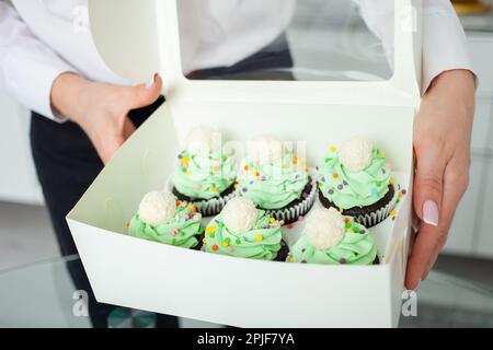 Il pasticciere professionale preparò tortini sotto forma di alberi di Natale. Dolci deliziosi per ogni vacanza, regalo. Panna montata verde. Mani Foto Stock